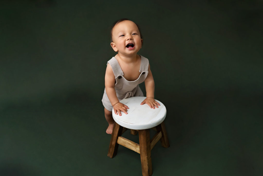 1 year old baby boy smiles whike using a stool to help him stand up.