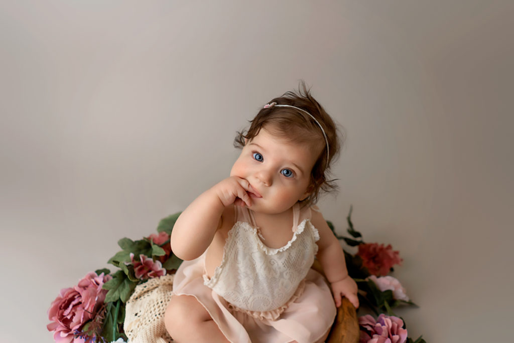 Studio portrait of a baby girl sitting around flowers.