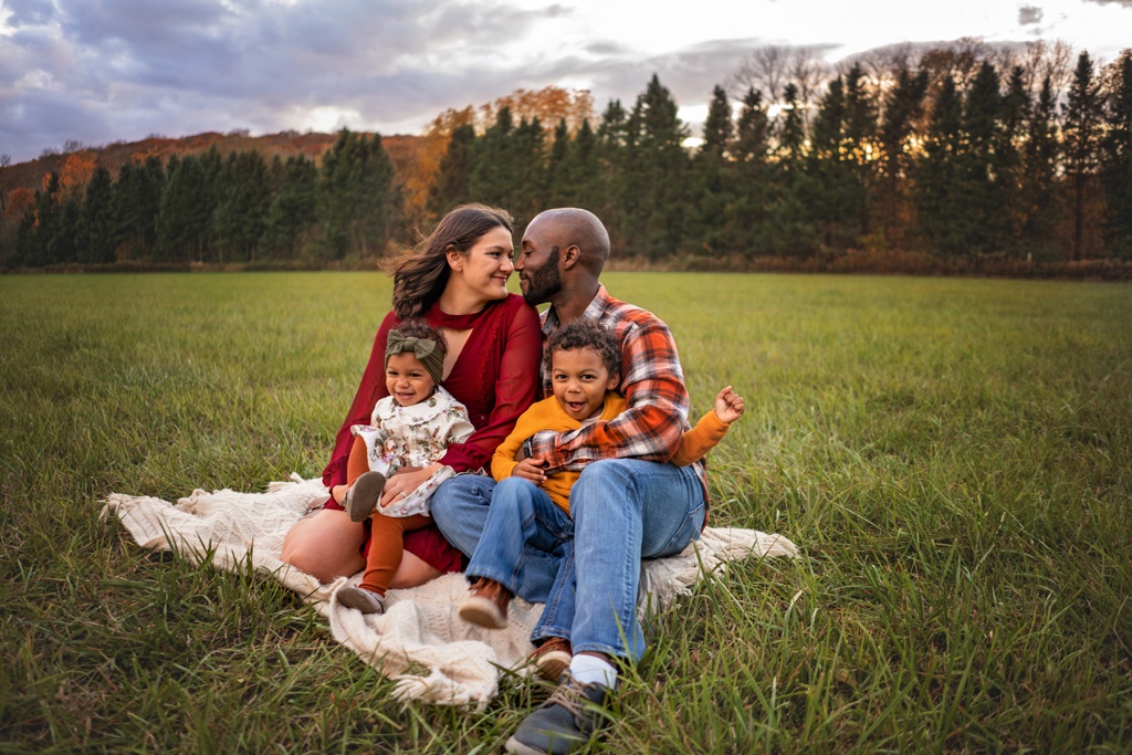 Family of 4 portrait photography in an open grassy field. Family is all sitting on a cream colored blanket