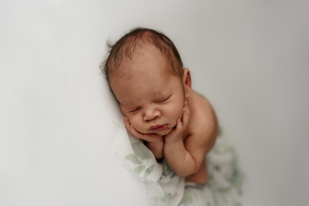 Sleeping newborn baby with hands curled under his chin during newborn studio photography