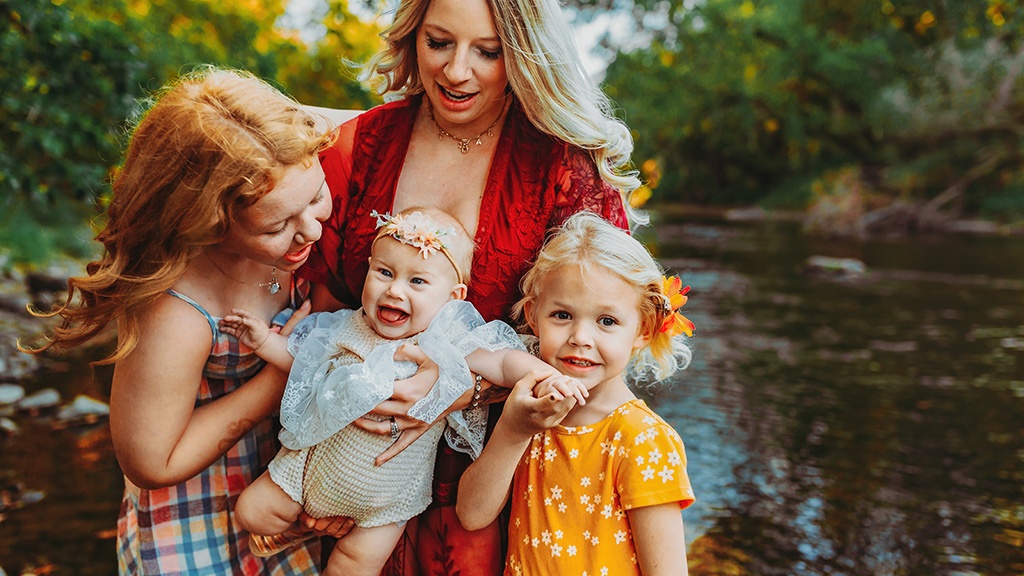 A mother and her 3 daughters are standing in a river smiling and playing during their photo session in Owatonna, MN.