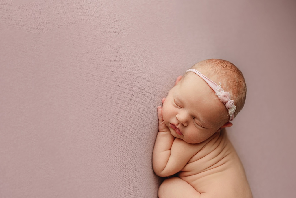 Newborn girl sleeping curled up on a pink backdrop